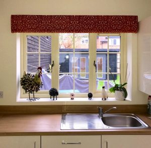 Upholstered decorative pelmet in a burnt orange textured pattern with voile roller blind behind