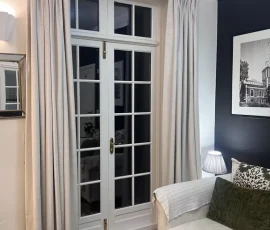 Triple pinch pleat made to measure curtains in Ashley Wilde Dakota fabric, a rich textured velvet, in colour Fog, a classic light neutral. Installed in a Welyn home with an Art Deco interior