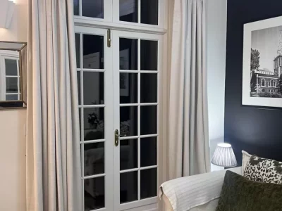 Triple pinch pleat made to measure curtains in Ashley Wilde Dakota fabric, a rich textured velvet, in colour Fog, a classic light neutral. Installed in a Welyn home with an Art Deco interior